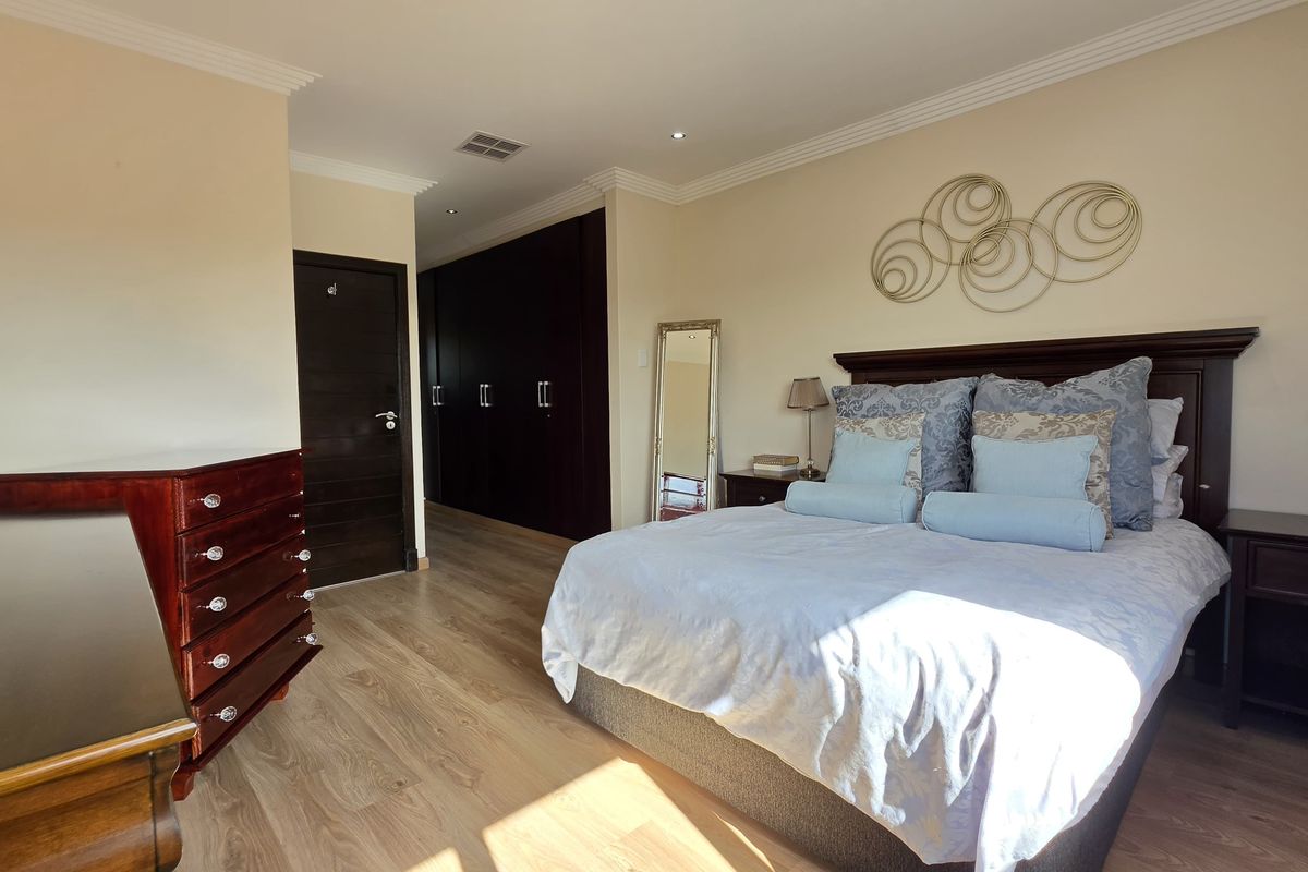 Spacious bedroom featuring light laminate flooring, extensive dark wood built-in cupboards, and elegant crown molding with recessed lighting.