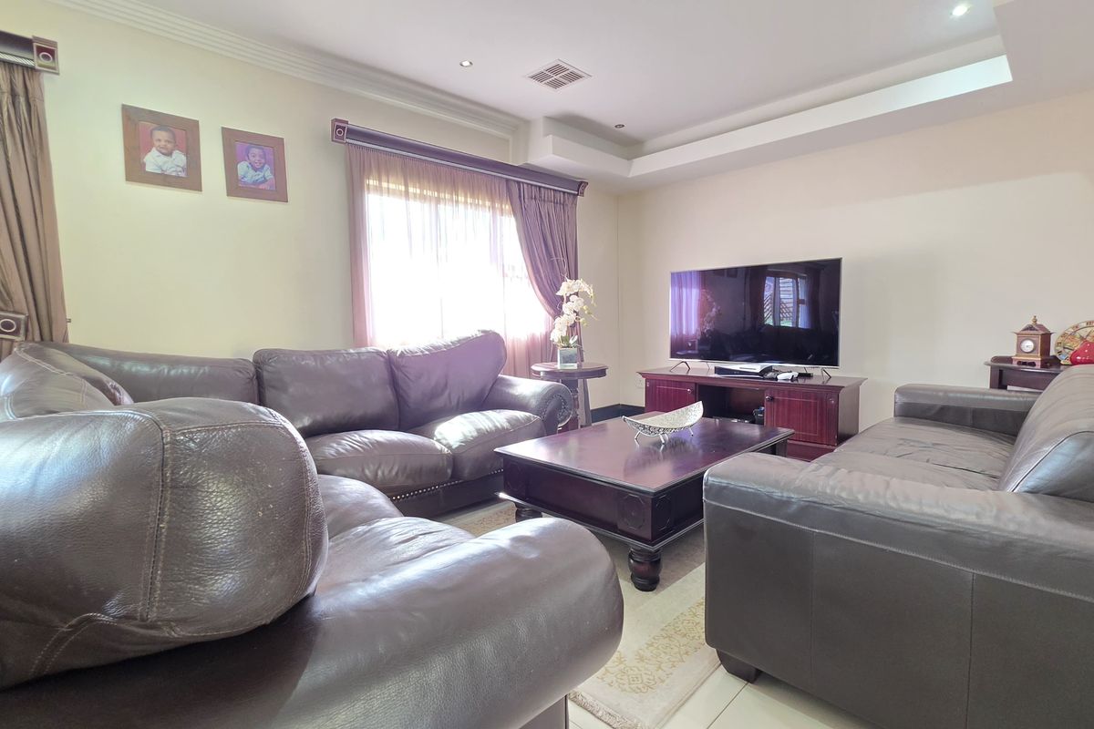 A comfortable living room featuring tiled flooring, recessed ceiling detail with downlights, and large windows with fitted curtain rails.