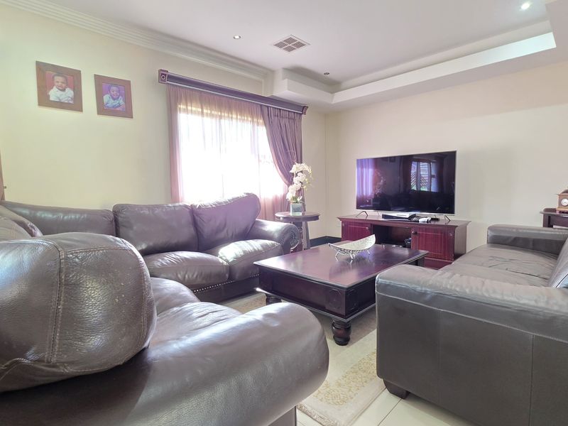 A comfortable living room featuring tiled flooring, recessed ceiling detail with downlights, and large windows with fitted curtain rails.