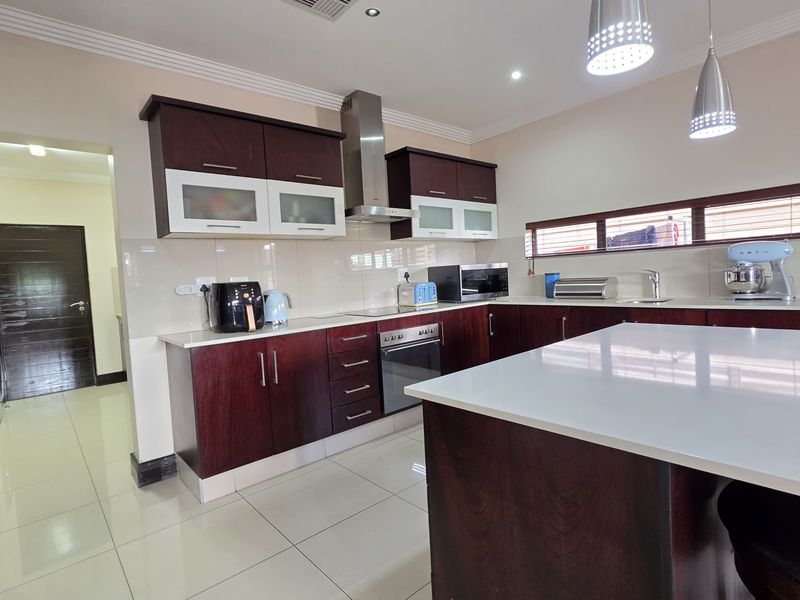 Modern kitchen featuring dark wood cabinetry, white stone countertops, a central island, and integrated stainless steel appliances with tiled flooring.