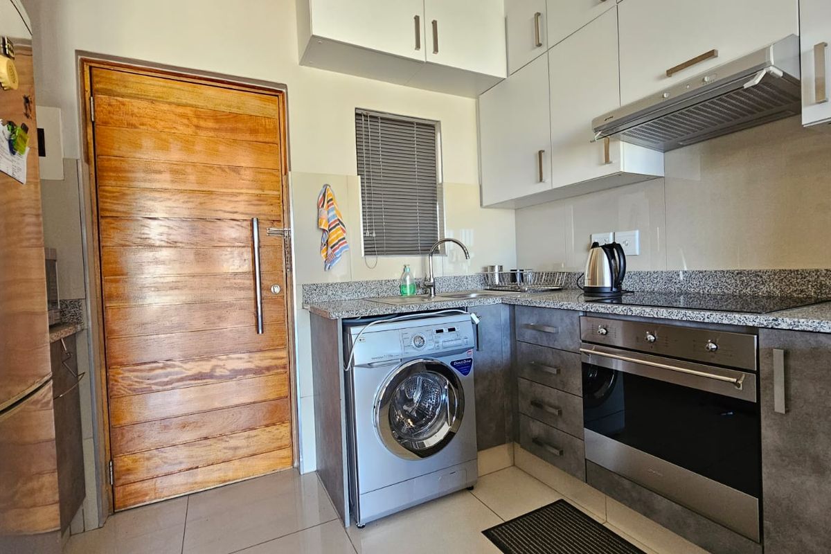 Compact modern kitchen featuring granite countertops, built-in oven, electric hob, extractor fan, and ample cabinetry with integrated laundry space.