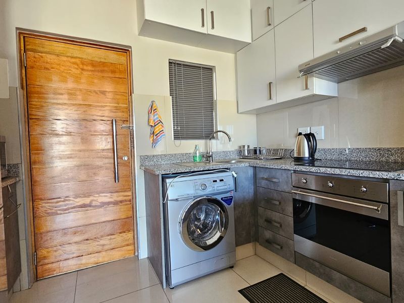 Compact modern kitchen featuring granite countertops, built-in oven, electric hob, extractor fan, and ample cabinetry with integrated laundry space.
