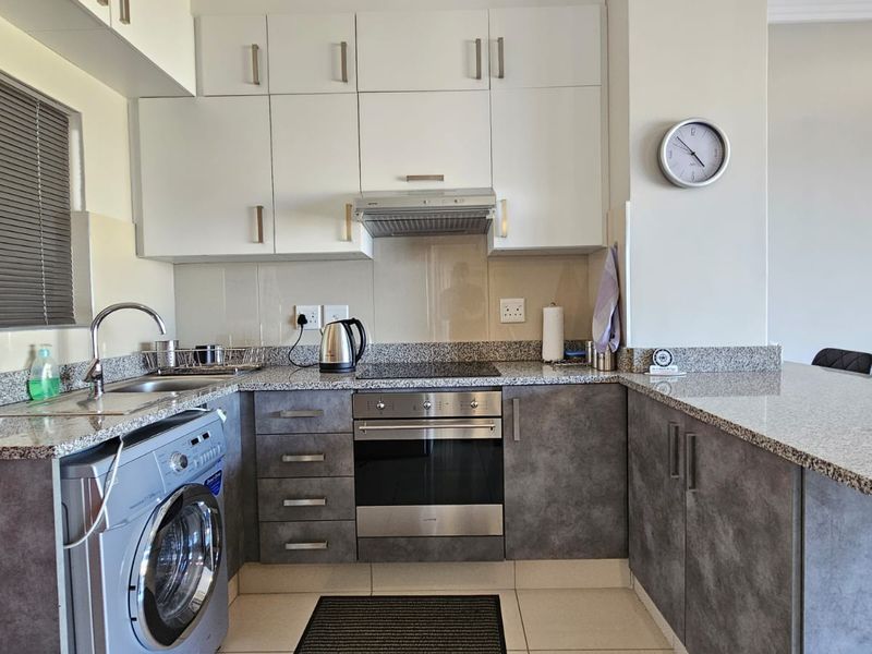 Modern kitchen featuring granite countertops, built-in oven, electric hob, extractor fan, and ample upper and lower cabinetry with integrated laundry space.
