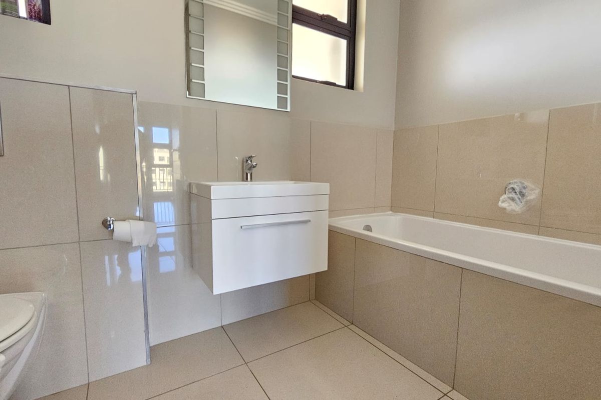 A modern, neutral-toned bathroom featuring a wall-mounted vanity, bathtub, and integrated toilet with wall-mounted flush plate.