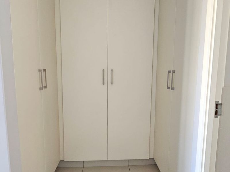 A clean and well-maintained hallway featuring neutral tiled flooring and extensive built-in cupboard storage.