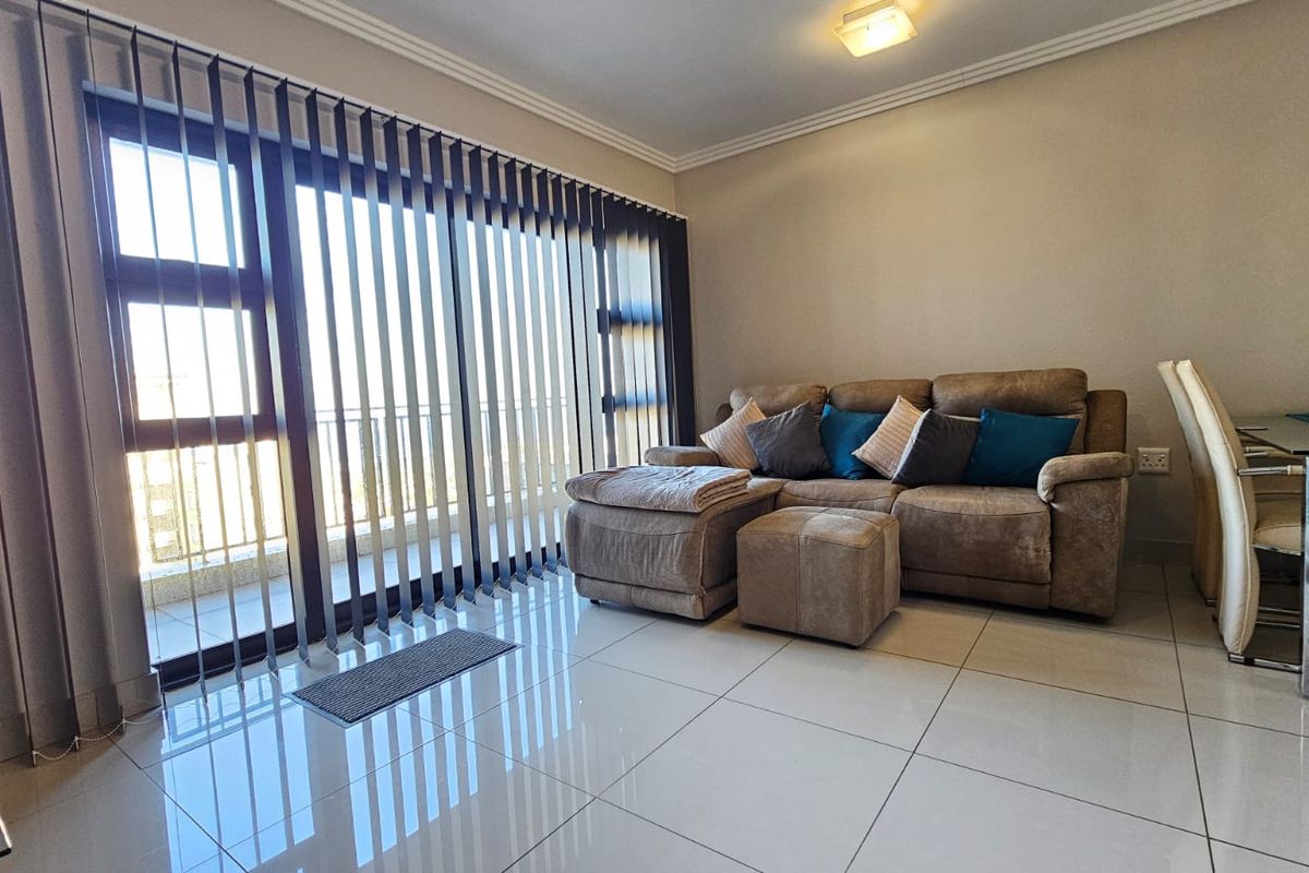 A bright living room featuring large sliding glass doors with vertical blinds, polished tiled flooring, and crown molding, offering a clean and well-maintained living space.