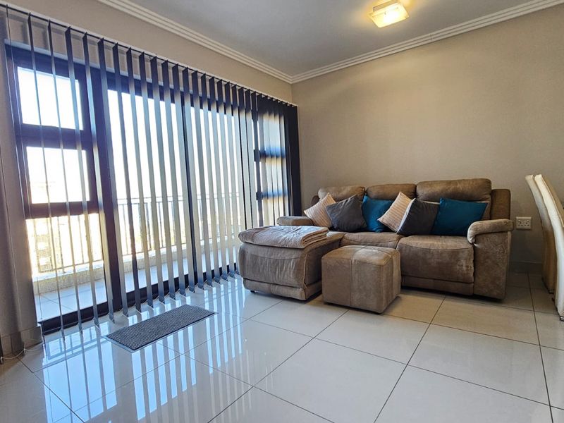 A bright living room featuring large sliding glass doors with vertical blinds, polished tiled flooring, and crown molding, offering a clean and well-maintained living space.
