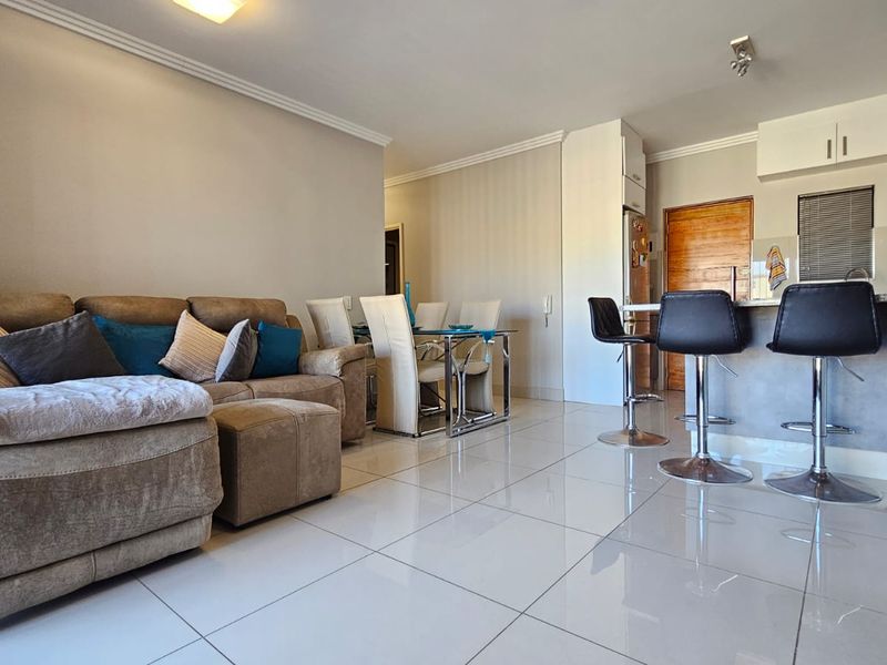 Open plan living and dining area featuring tiled flooring, a breakfast bar, and integrated kitchen cabinetry in a well-maintained apartment setting.