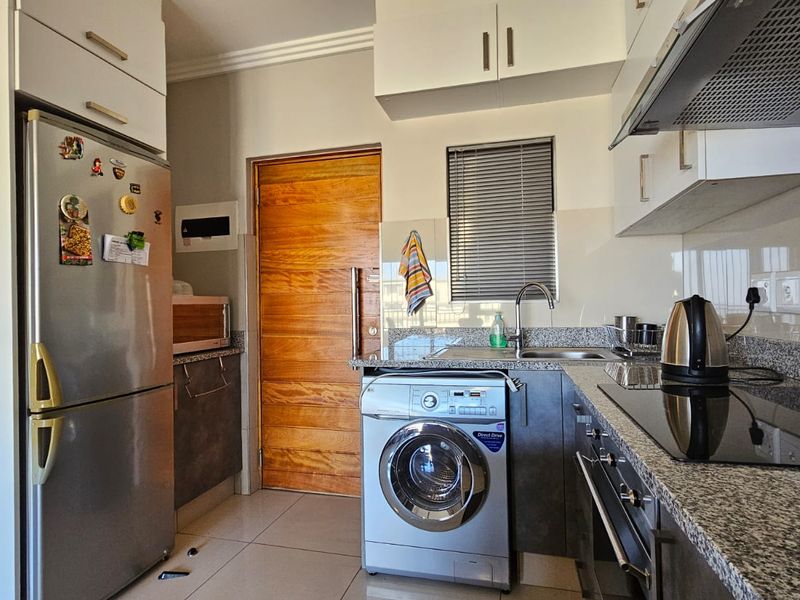A functional kitchen featuring granite countertops, built-in cabinetry, an integrated oven and hob, and space for a washing machine.