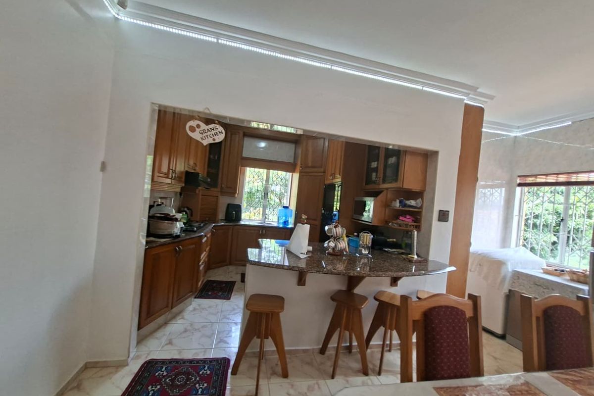 Open plan kitchen featuring wooden cabinetry, granite countertops, and a breakfast bar, seamlessly connected to the dining area with tiled flooring throughout.