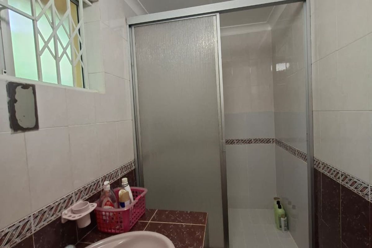 A dated bathroom featuring a shower enclosure, vanity basin, and tiled finishes, requiring minor repairs to electrical fixtures.