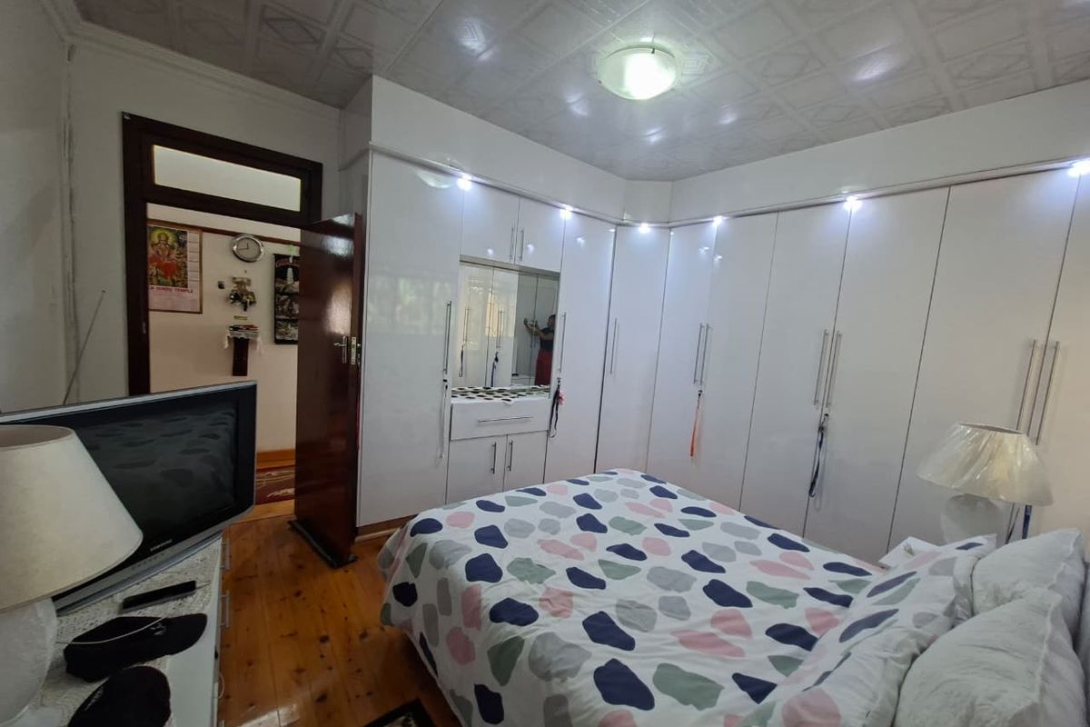 A well-maintained bedroom featuring extensive white built-in cupboards with integrated lighting, polished hardwood flooring, and decorative ceiling tiles.