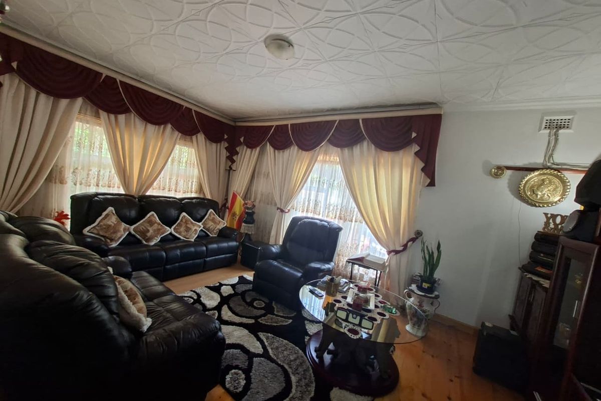 A living room featuring timber flooring and decorative ceiling tiles, offering a traditional layout with ample natural light through window treatments.