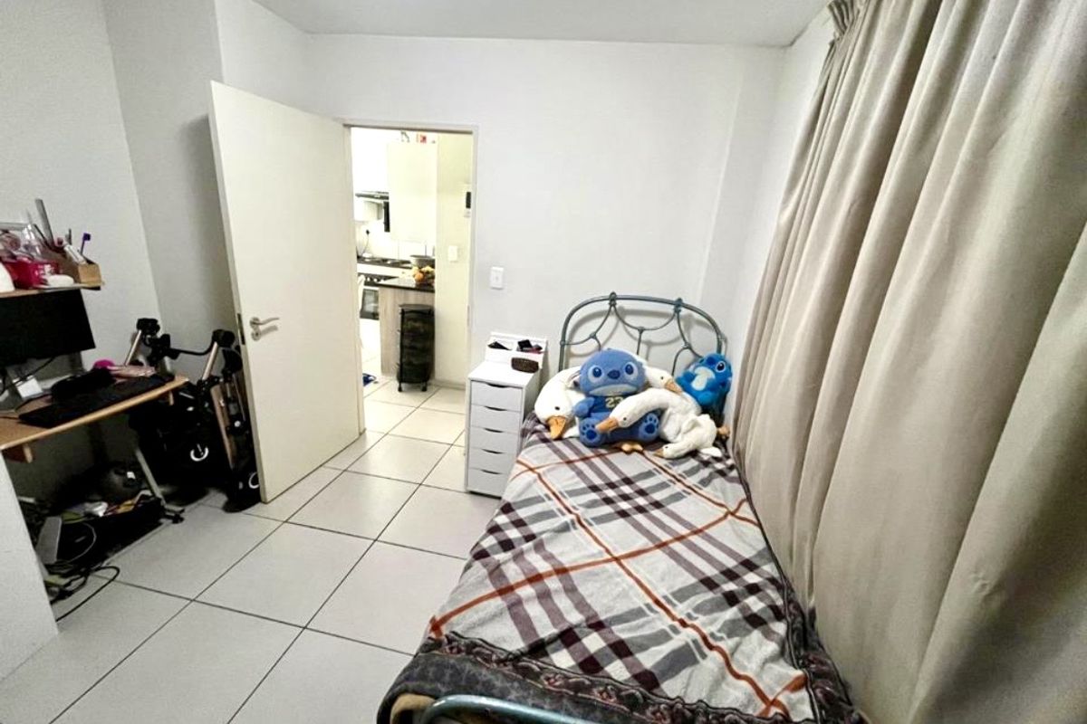 A functional bedroom featuring tiled flooring and neutral walls, with an open doorway leading to the kitchen area.