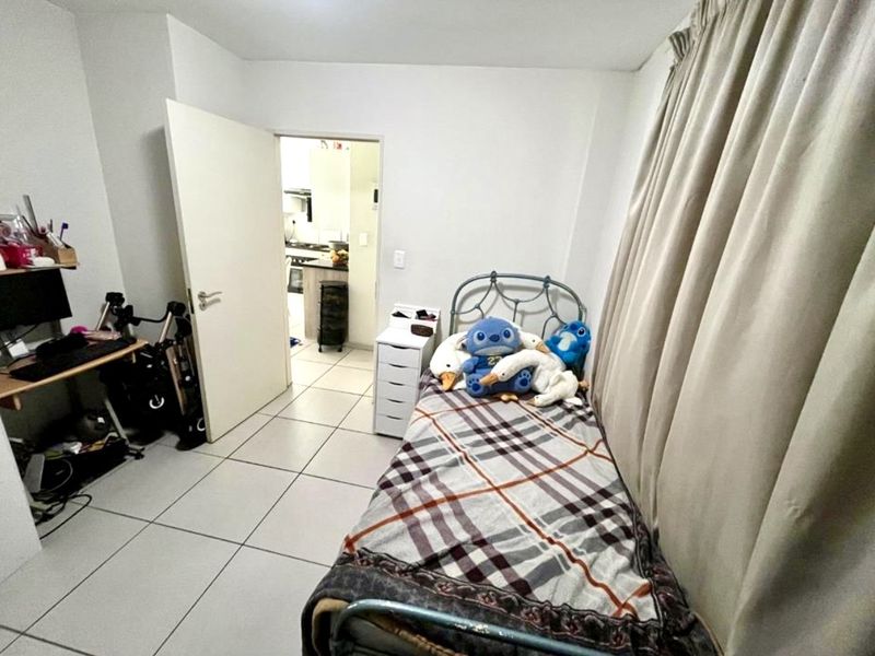 A functional bedroom featuring tiled flooring and neutral walls, with an open doorway leading to the kitchen area.