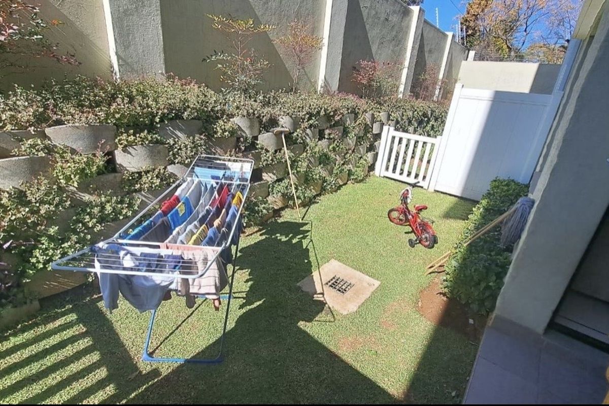A private rear garden area featuring a lawn, retaining wall, and boundary fencing, providing a compact outdoor space for the apartment.