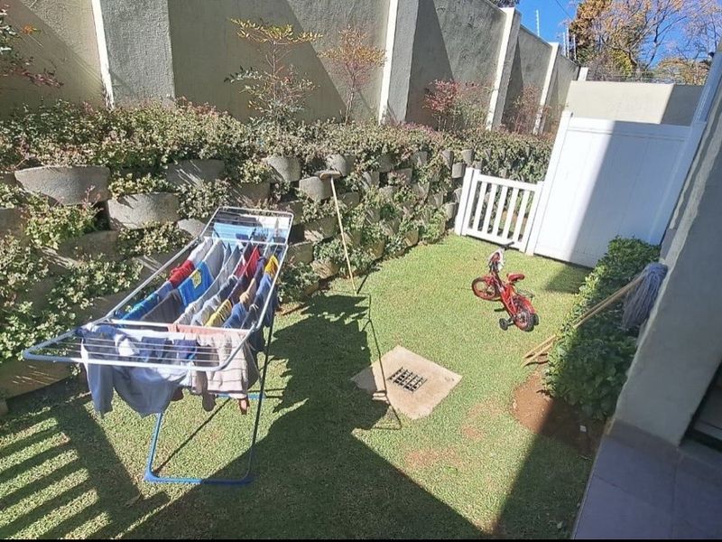 A private rear garden area featuring a lawn, retaining wall, and boundary fencing, providing a compact outdoor space for the apartment.