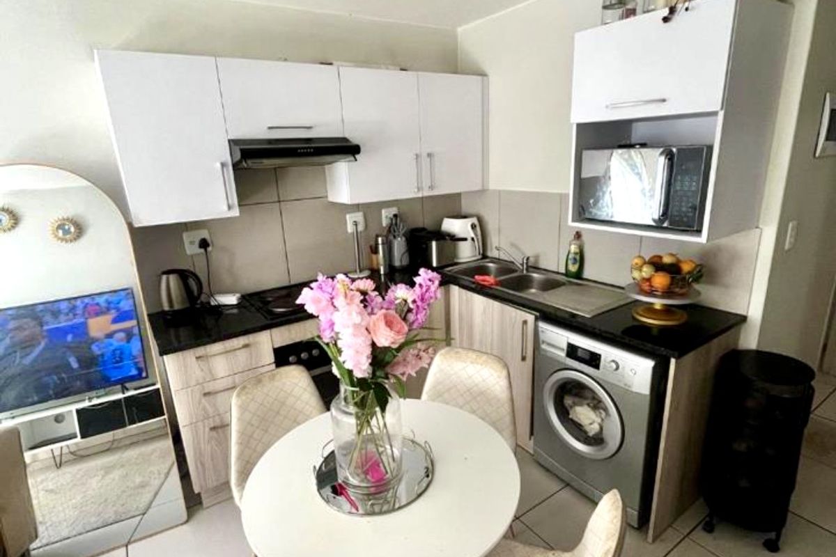 Compact kitchen featuring white cabinetry, dark countertops, integrated appliances, and tiled flooring, designed for efficient use of space in an apartment setting.