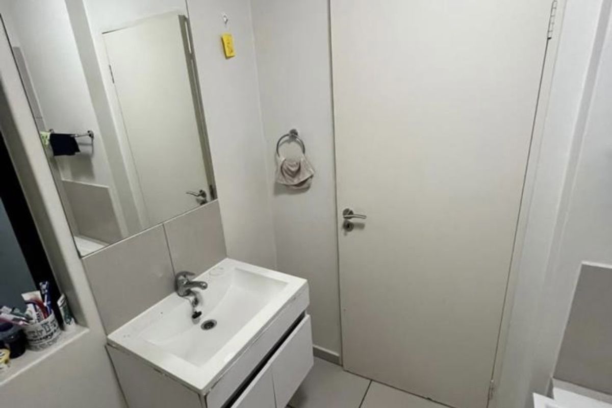A clean and functional bathroom featuring a modern wall-mounted vanity with a ceramic basin, large mirror, and neutral floor tiling.