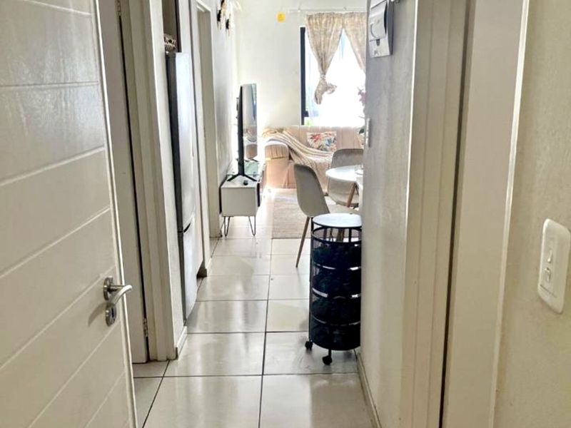 A narrow hallway with tiled flooring leading into an open-plan living area, featuring standard internal doors and an accessible electrical distribution board.