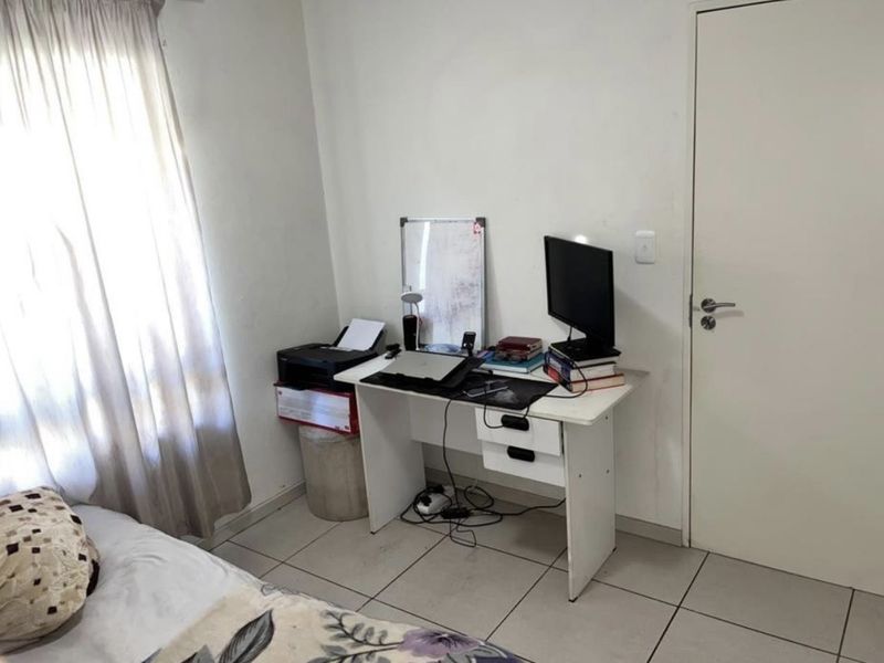 A functional bedroom featuring tiled flooring and neutral wall finishes, currently utilized as a workspace.