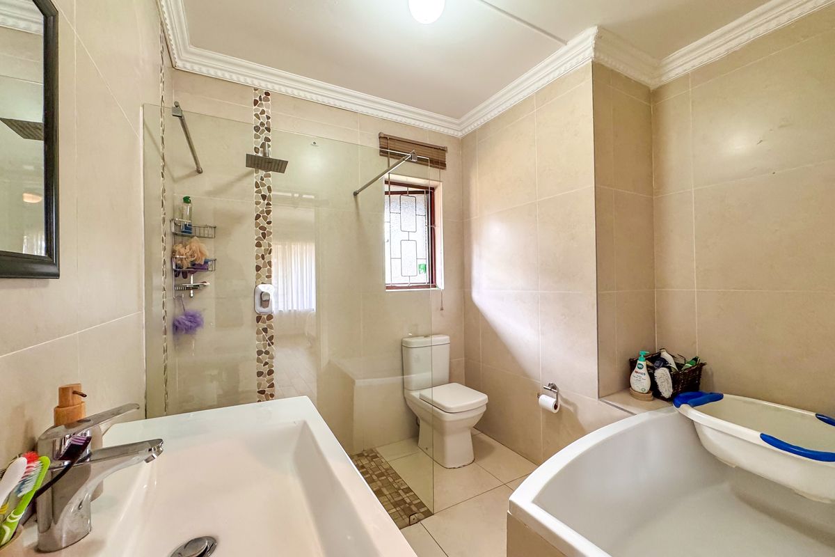 Modern bathroom featuring a walk-in shower with glass screen, rain shower head, built-in bathtub, and neutral floor-to-ceiling tiling with decorative mosaic accents.