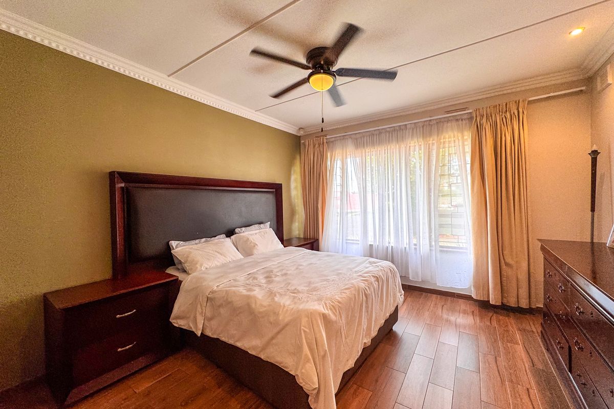 A well-maintained bedroom featuring laminate flooring, crown molding, and a ceiling fan, with large windows fitted with security bars.