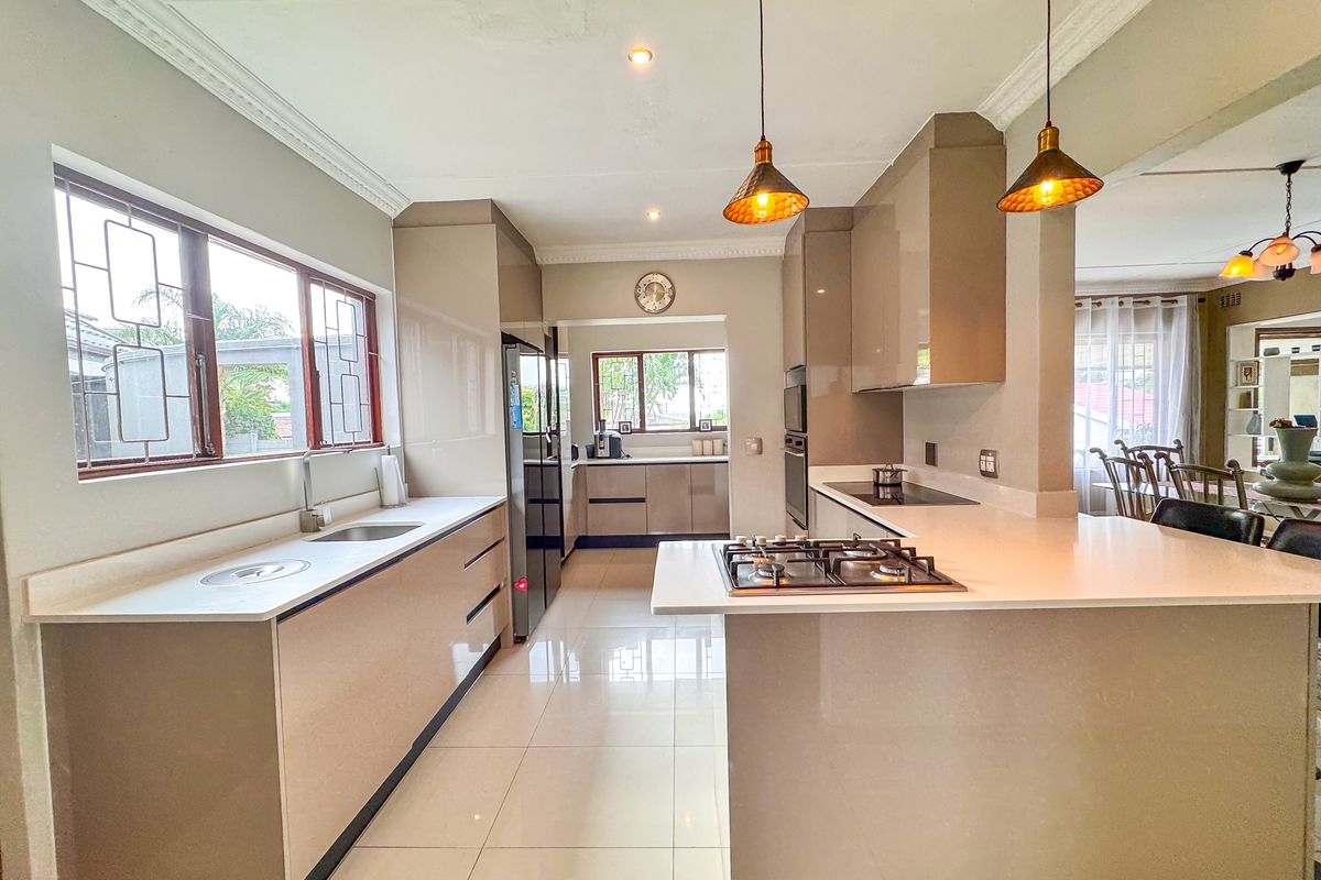 Modern kitchen featuring sleek high-gloss cabinetry, stone countertops, a gas hob, and integrated appliances, flowing seamlessly into the adjacent dining area.