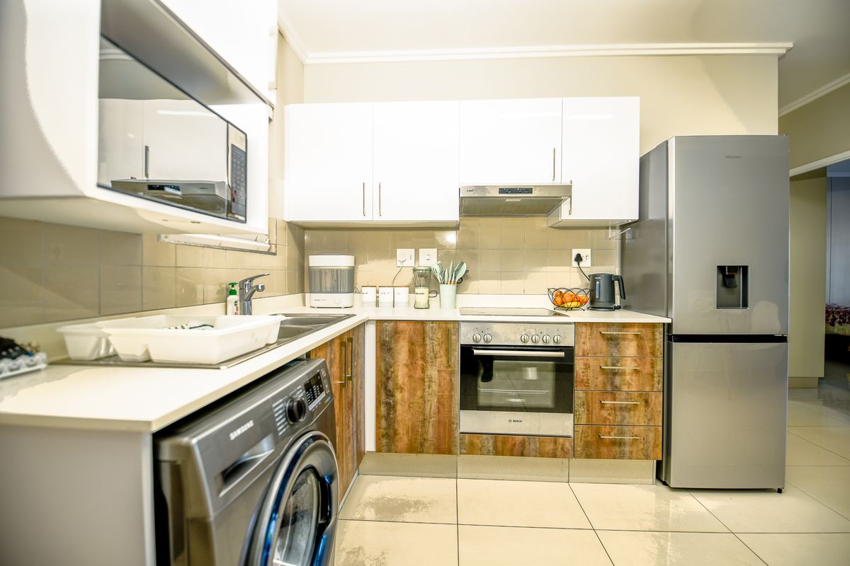 Compact kitchen featuring white upper cabinets, wood-look lower cabinetry, built-in oven, hob, extractor fan, and tiled flooring.