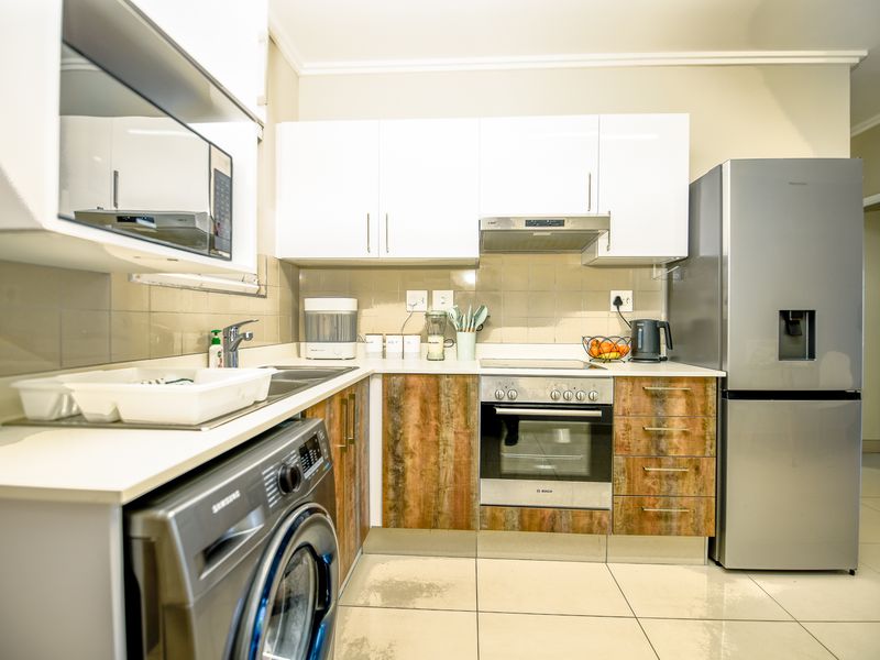 Compact kitchen featuring white upper cabinets, wood-look lower cabinetry, built-in oven, hob, extractor fan, and tiled flooring.