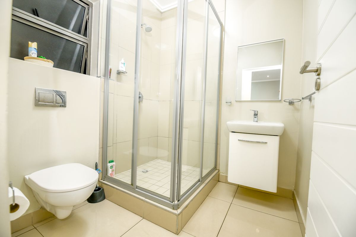 A modern, compact bathroom featuring a wall-mounted toilet, a glass shower enclosure, and a sleek wall-mounted vanity with a basin.