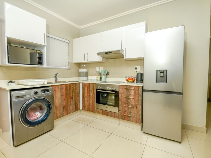 A functional kitchen featuring white upper cabinets, wood-look lower cabinetry, tiled flooring, and integrated appliances including an oven, hob, and extractor fan.
