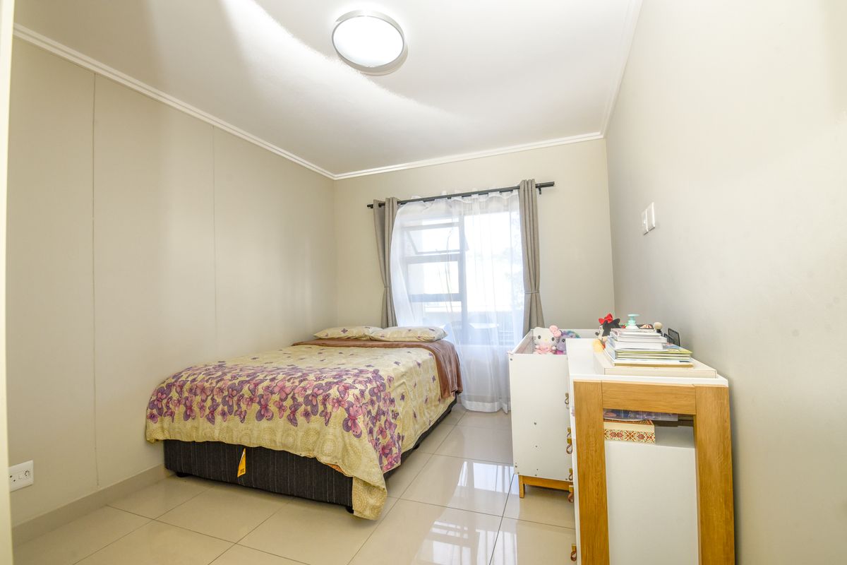 A well-maintained bedroom featuring neutral wall tones, large format floor tiles, and a window with fitted curtain hardware.