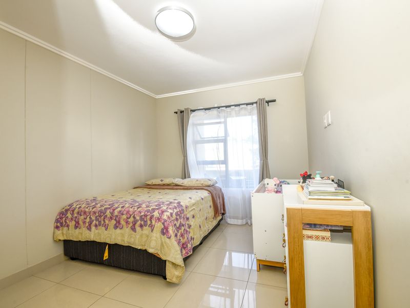 A well-maintained bedroom featuring neutral wall tones, large format floor tiles, and a window with fitted curtain hardware.
