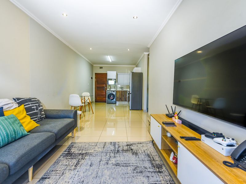 Open-plan living area featuring polished tile flooring, recessed lighting, and a compact integrated kitchen with laundry facilities.