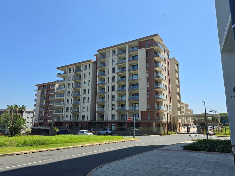 A modern multi-story apartment complex featuring glass balconies, brick and render facade, and a secure gated entrance.