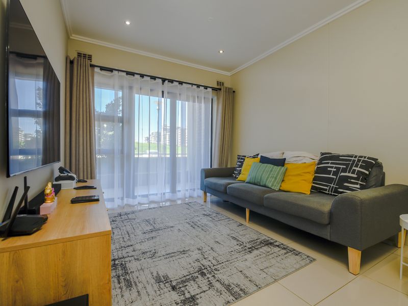 A bright and well-maintained living room featuring tiled flooring, recessed lighting, and a large sliding glass door providing access to the balcony.