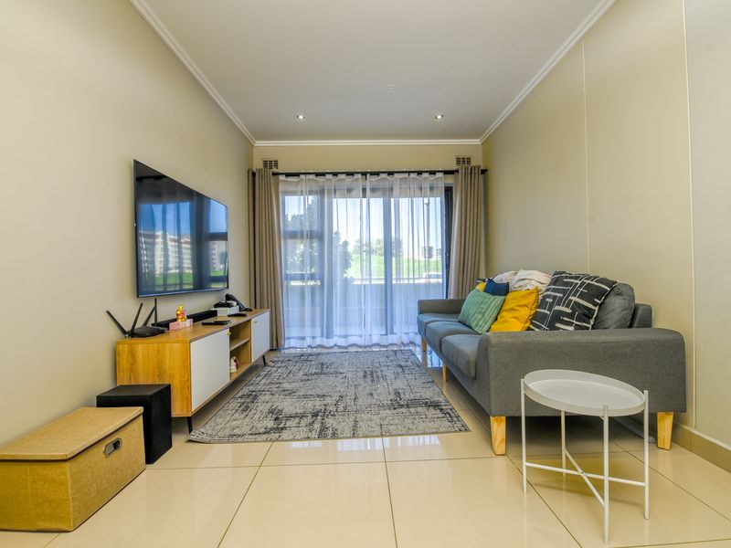 A well-maintained living room featuring large format floor tiles, recessed lighting, and a sliding glass door providing access to the outdoor area.