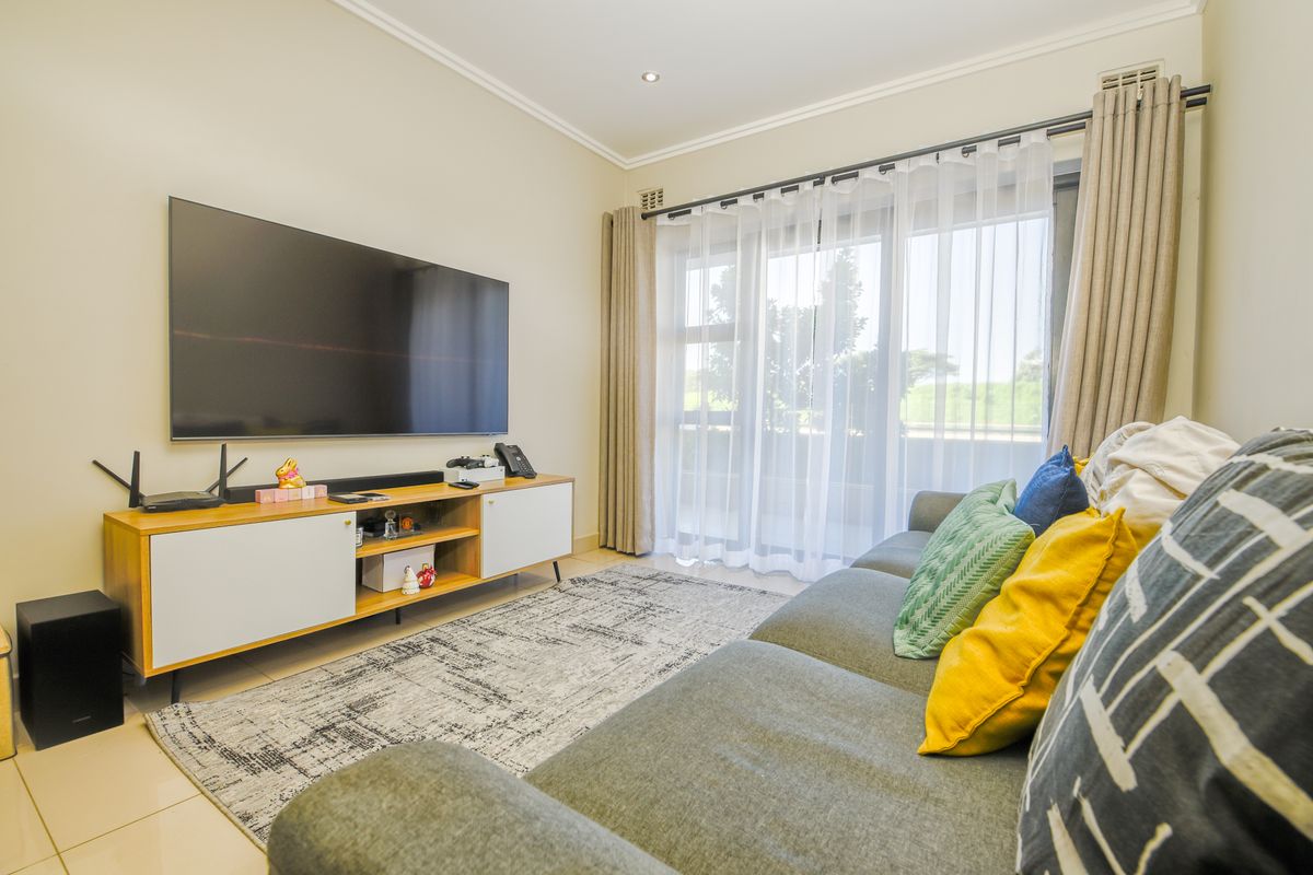 A well-maintained living room featuring tiled flooring, recessed downlighting, and a large sliding glass door providing access to the balcony.