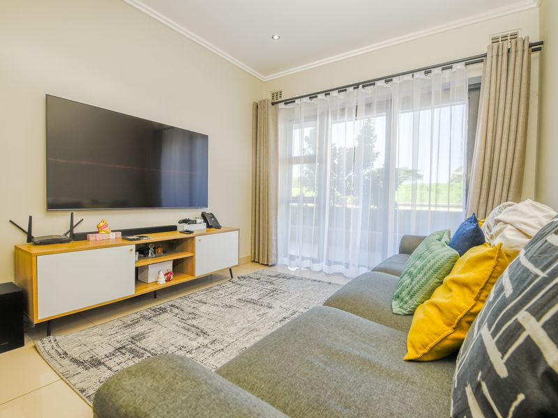 A well-maintained living room featuring tiled flooring, recessed downlighting, and a large sliding glass door providing access to the balcony.