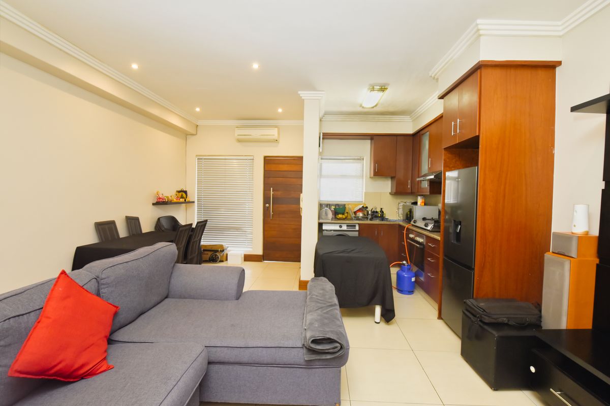 Open-plan living and kitchen area featuring tiled floors, built-in wooden cabinetry, integrated appliances, and an air conditioning unit.