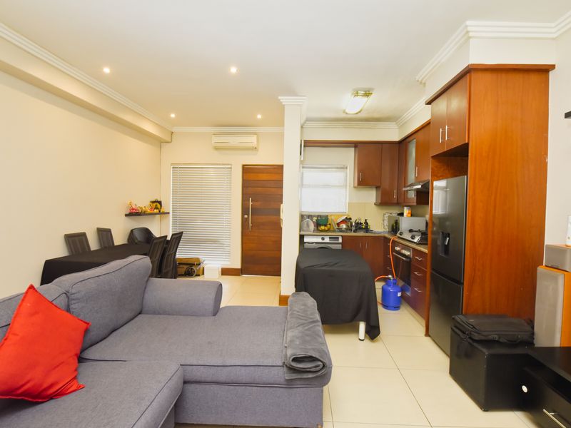 Open-plan living and kitchen area featuring tiled floors, built-in wooden cabinetry, integrated appliances, and an air conditioning unit.