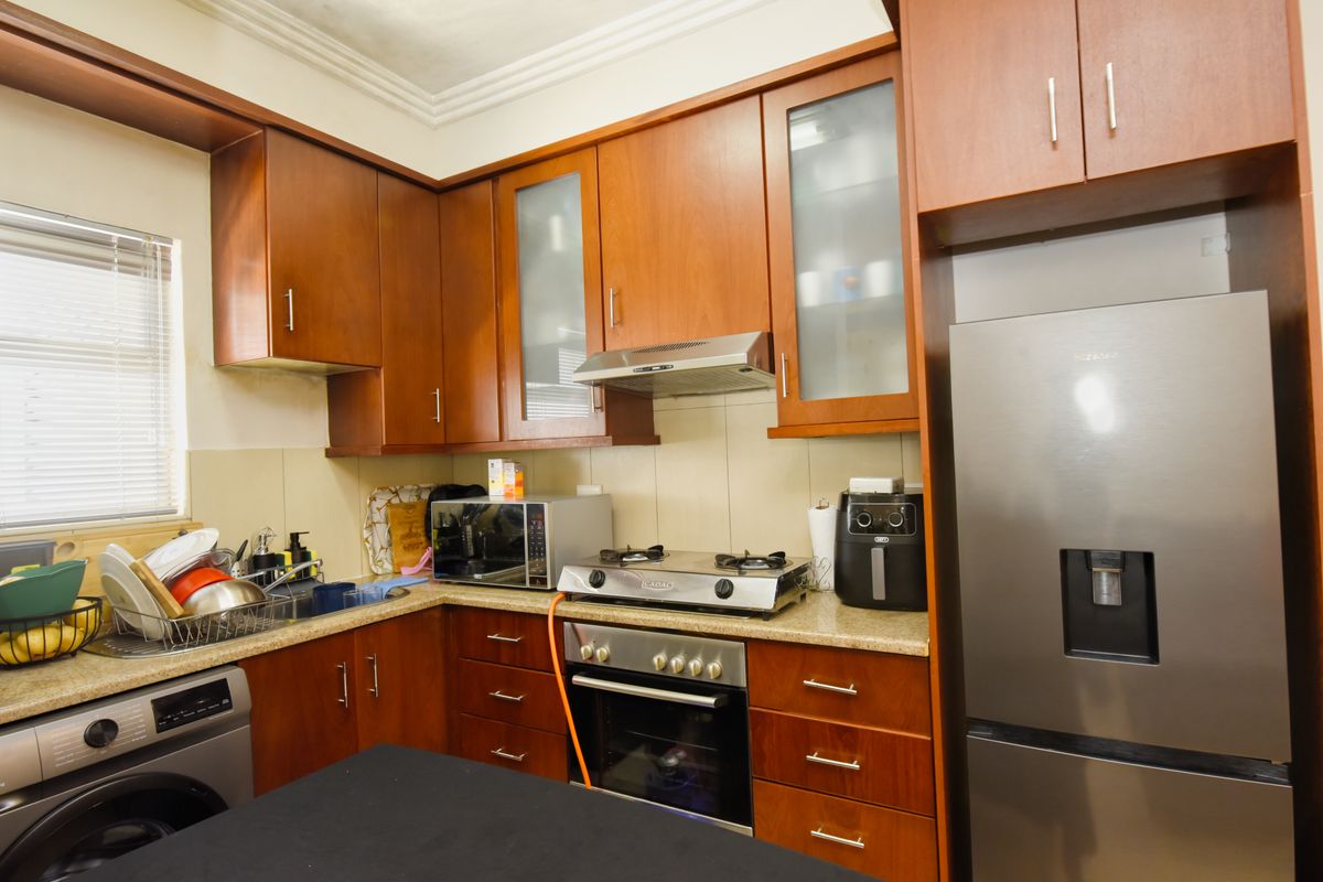 A functional kitchen featuring warm-toned wooden cabinetry, granite countertops, a built-in oven with gas hob, and an integrated washing machine space.