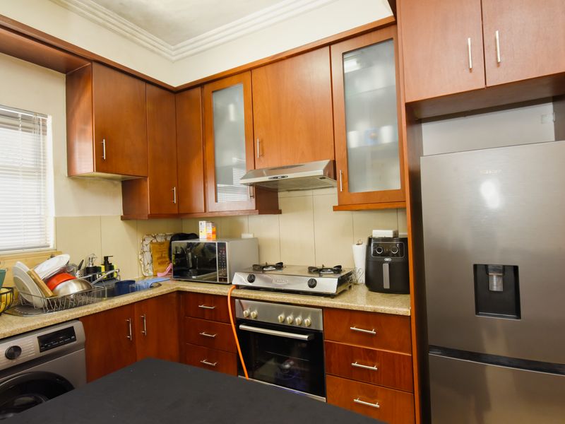 A functional kitchen featuring warm-toned wooden cabinetry, granite countertops, a built-in oven with gas hob, and an integrated washing machine space.