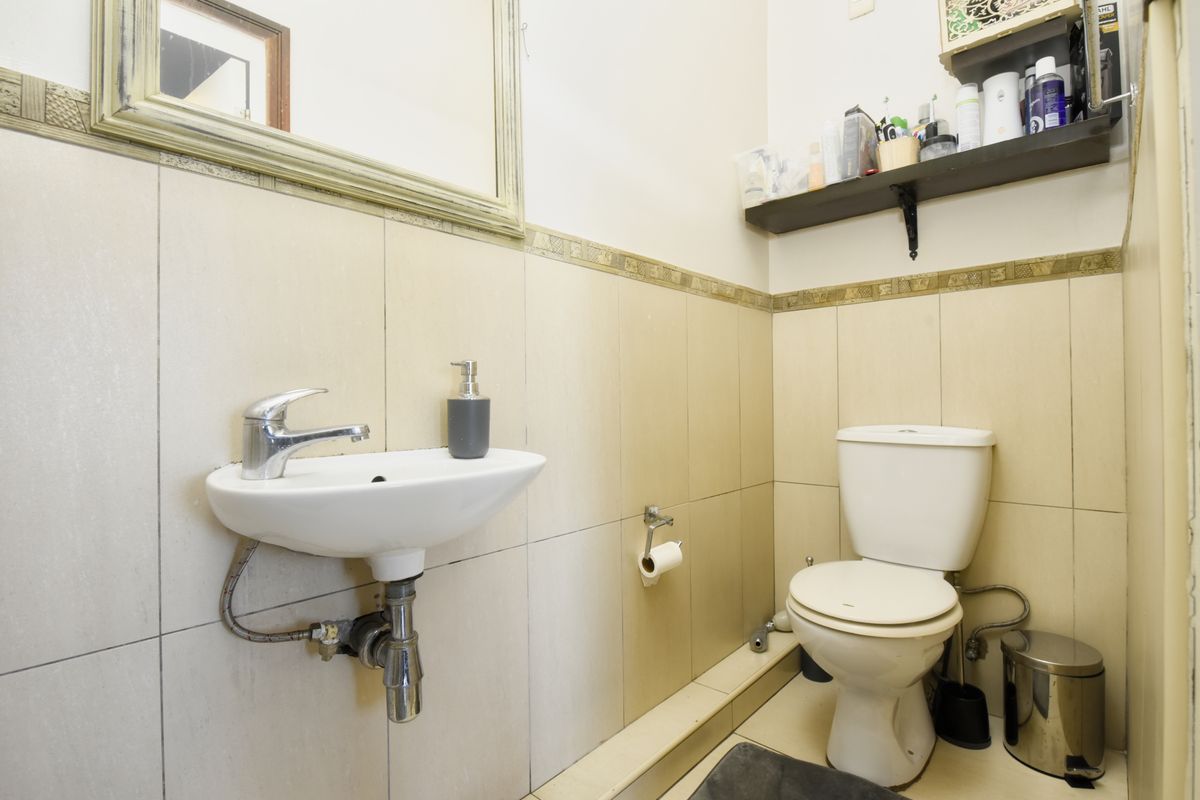 A compact bathroom featuring a wall-mounted basin with chrome mixer tap, a standard toilet, and neutral ceramic wall tiling with a decorative border.