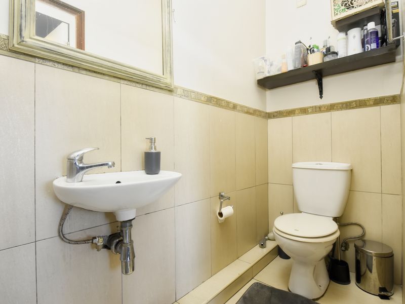 A compact bathroom featuring a wall-mounted basin with chrome mixer tap, a standard toilet, and neutral ceramic wall tiling with a decorative border.