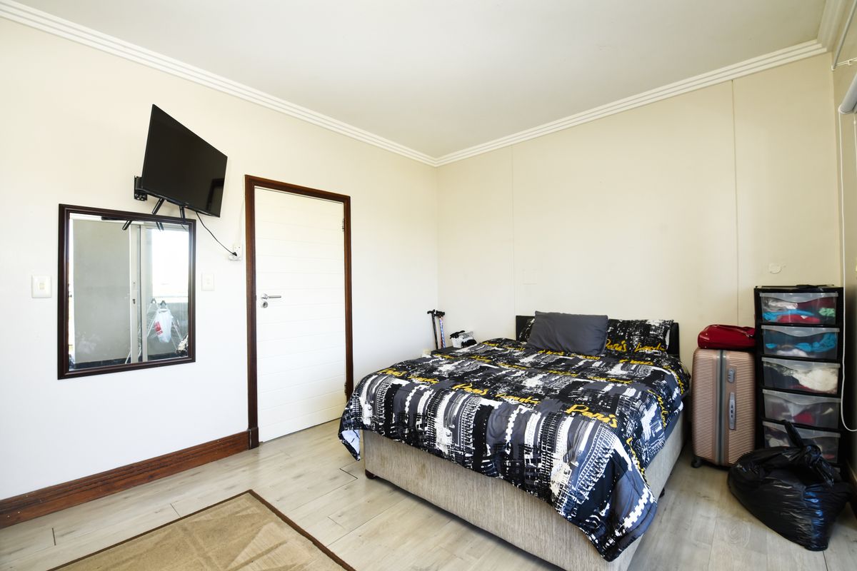 A functional bedroom featuring light-toned laminate flooring, white walls with crown molding, and a standard internal door.
