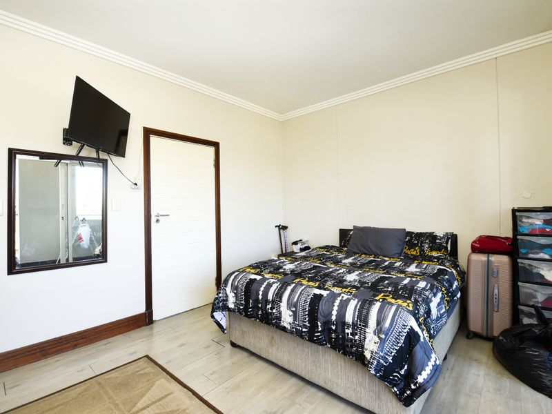 A functional bedroom featuring light-toned laminate flooring, white walls with crown molding, and a standard internal door.