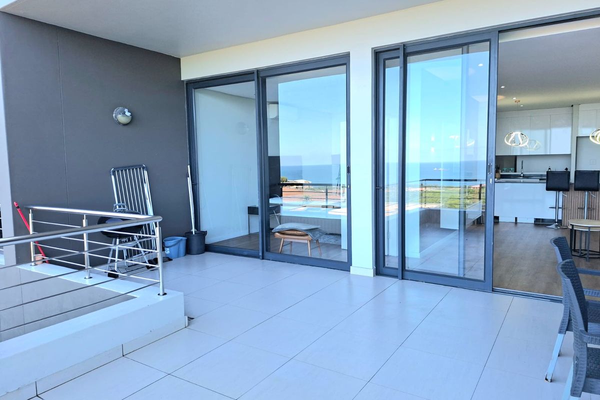 A spacious covered balcony featuring modern tiled flooring, stainless steel balustrades, and large sliding glass doors providing seamless access to the interior living area.