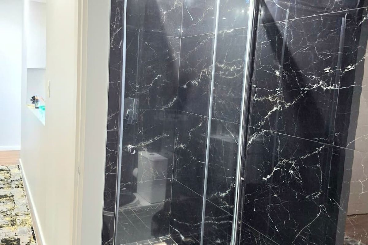 Modern bathroom featuring a sleek glass shower enclosure with striking black marble-effect wall tiling and high-quality finishes.